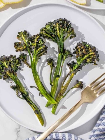 Roasted broccolini on a plate with lemon slices and a fork.