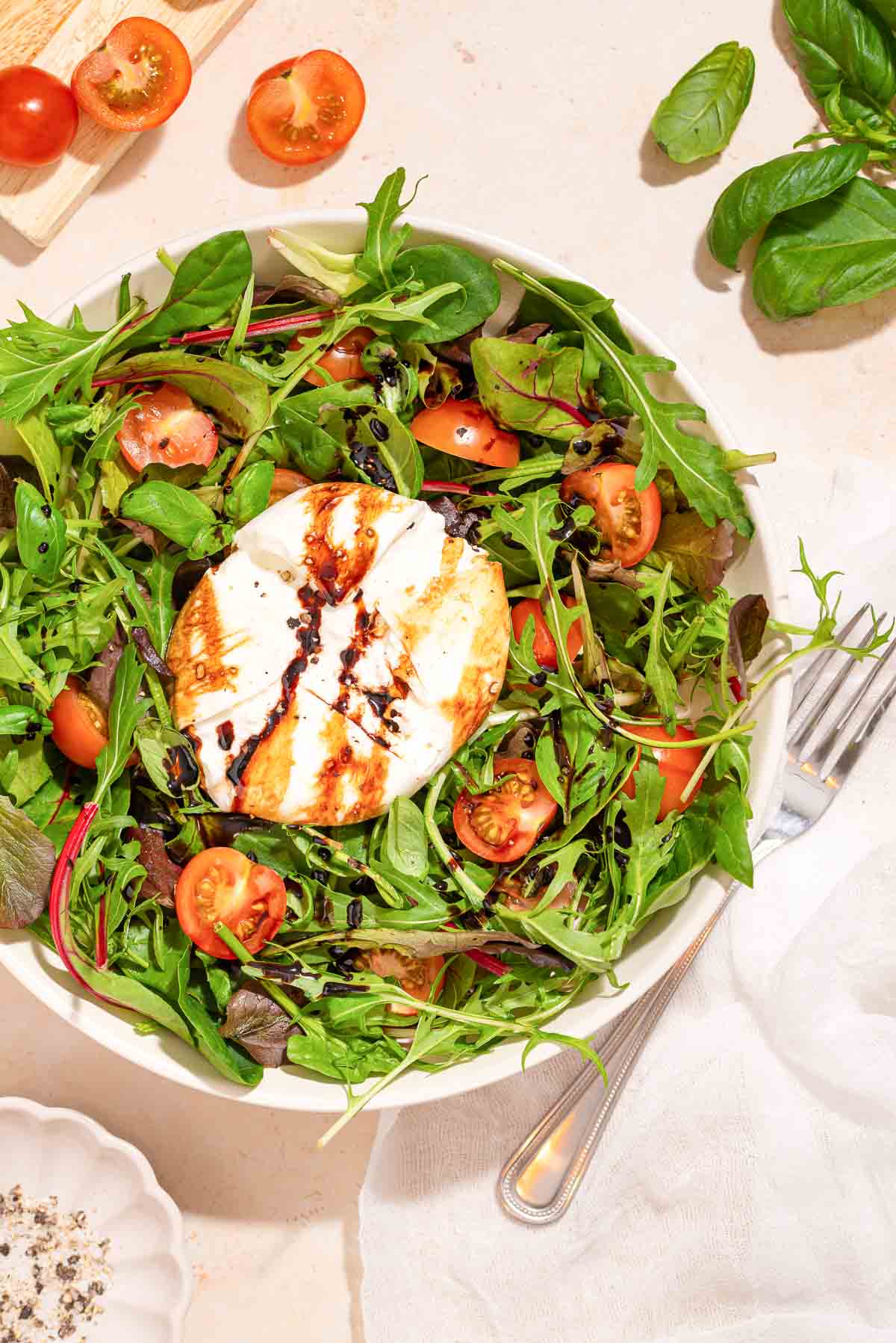 A white bowl with a burrata caprese salad on it.