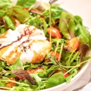 A bowl of burrata caprese salad with olive oil being poured over it.