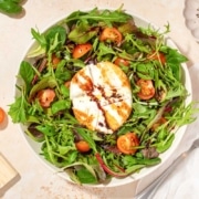 A salad with burrata and tomatoes on a white plate.
