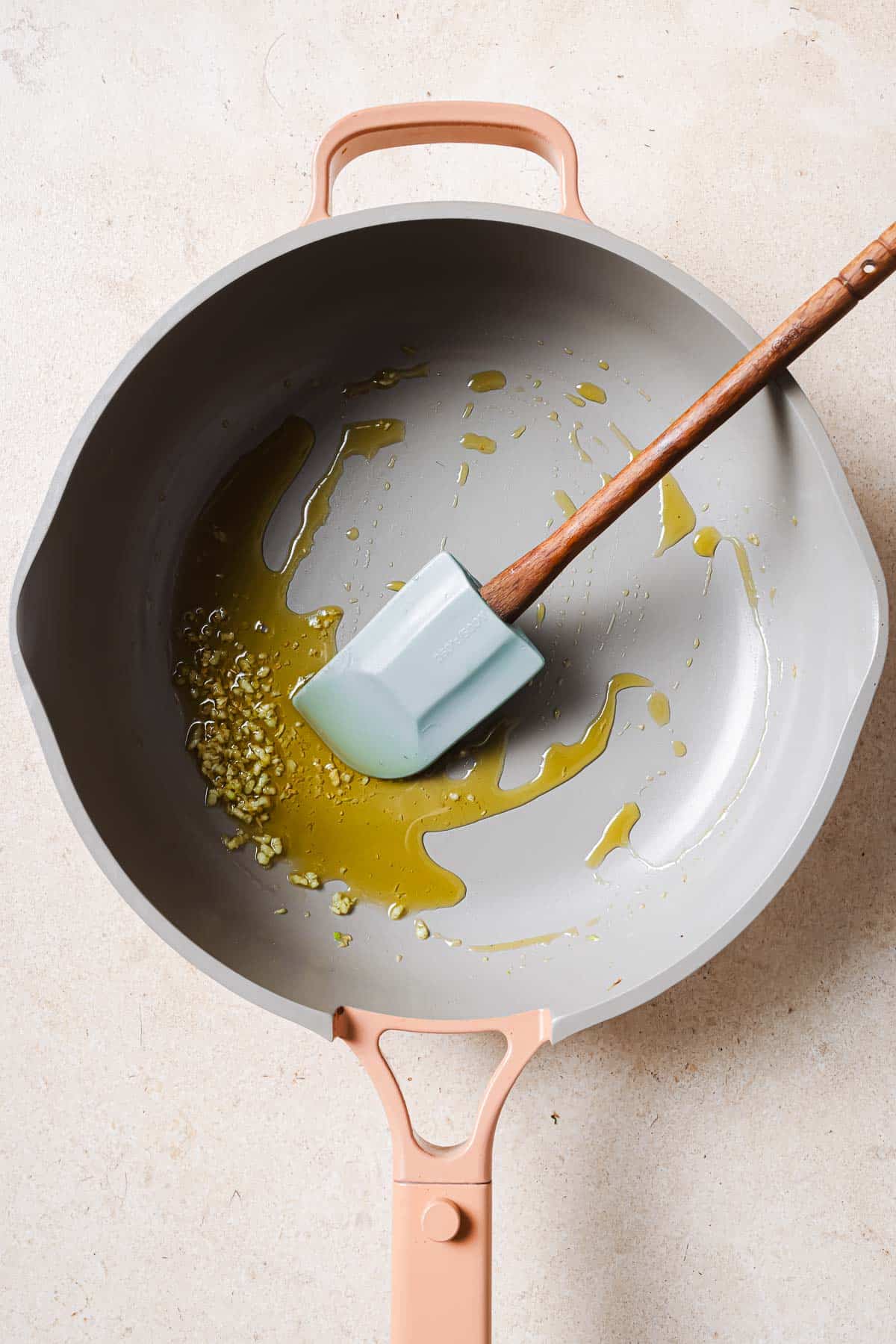 A frying pan with olive oil, garlic, and a wooden spatula.
