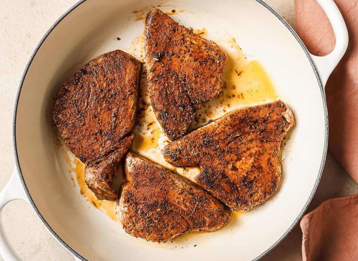 Blackened tuna steaks in a skillet on a pink linen.