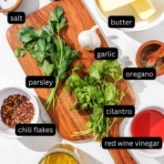 A cutting board with the labeled ingredients for chimichurri butter on it.