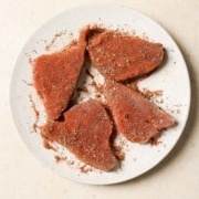 Four tuna steaks coated in a blackening spice on a white plate.