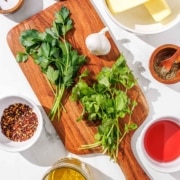 A cutting board with the ingredients for chimichurri butter on it.