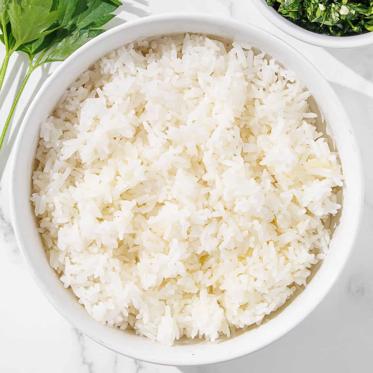 White rice in a bowl next to a bowl of parsley.