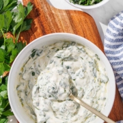 A bowl of chimichurri aioli with a spoon beside a blue and white linen.