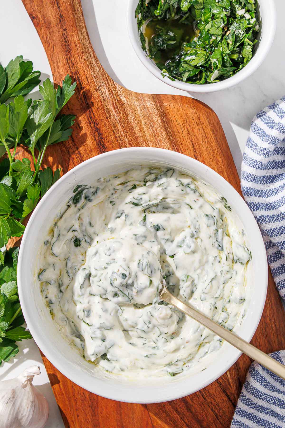 A bowl of chimichurri aioli with a spoon beside a blue and white linen.