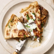 A plate of carne asada quesadillas with cheese and sour cream.