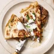 A plate of carne asada quesadillas with cheese and sour cream.