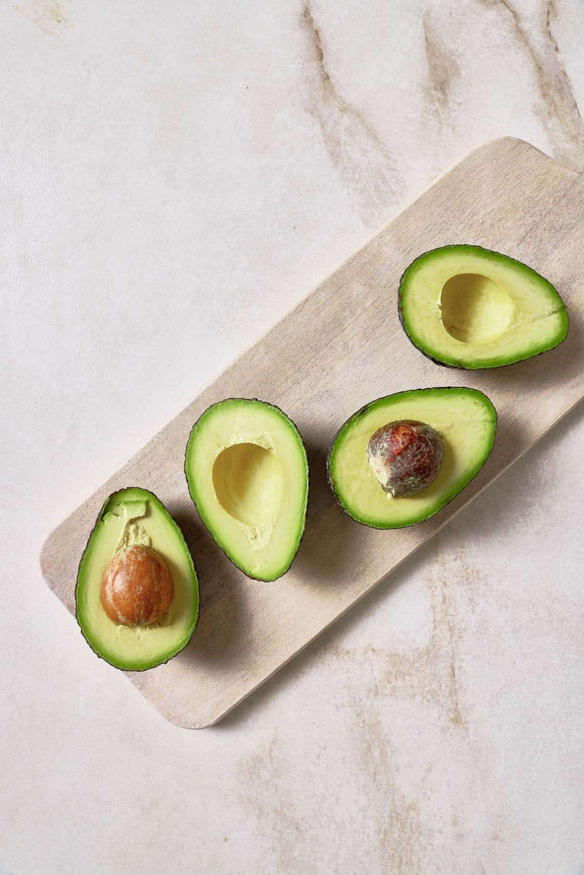 Four avocados on a wooden cutting board.