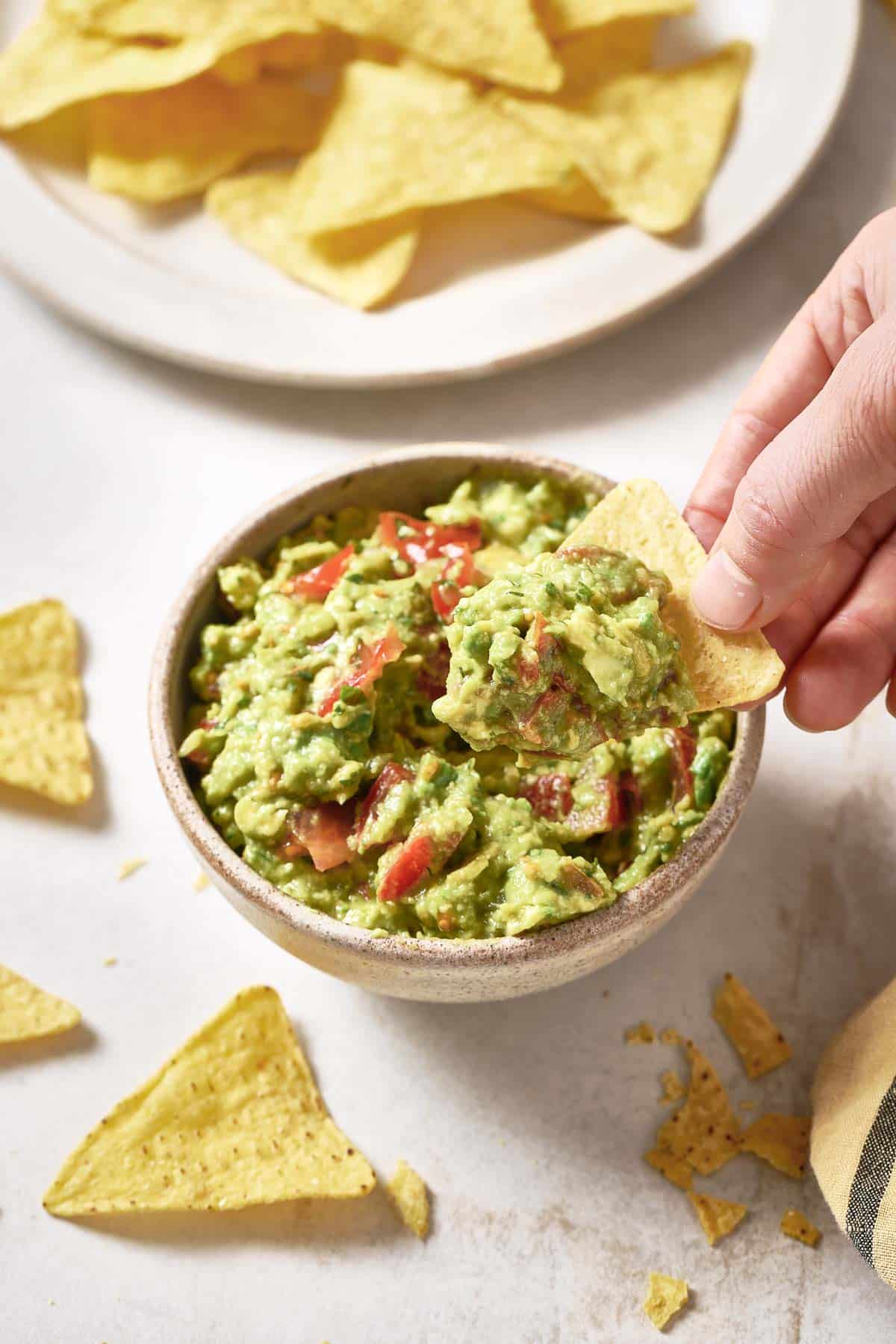 A person dipping chips into a bowl of 4-ingredient guacamole.