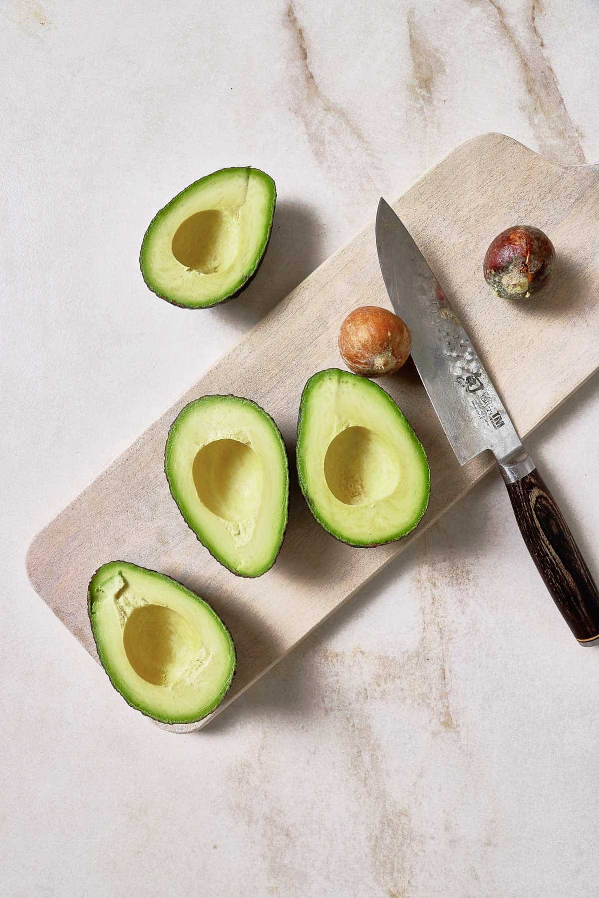 Avocados on a cutting board with a knife.