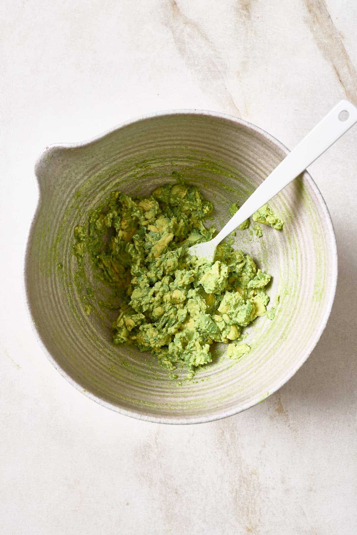 Mashed avocados in a white bowl with a spoon.