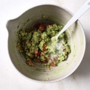 Salt is added to guacamole in a bowl with a spoon.