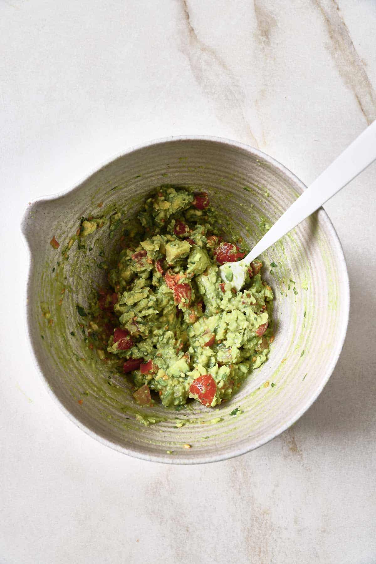 Guacamole in a white bowl with a spoon.
