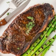 A cooked blackened steak with asparagus on a plate.