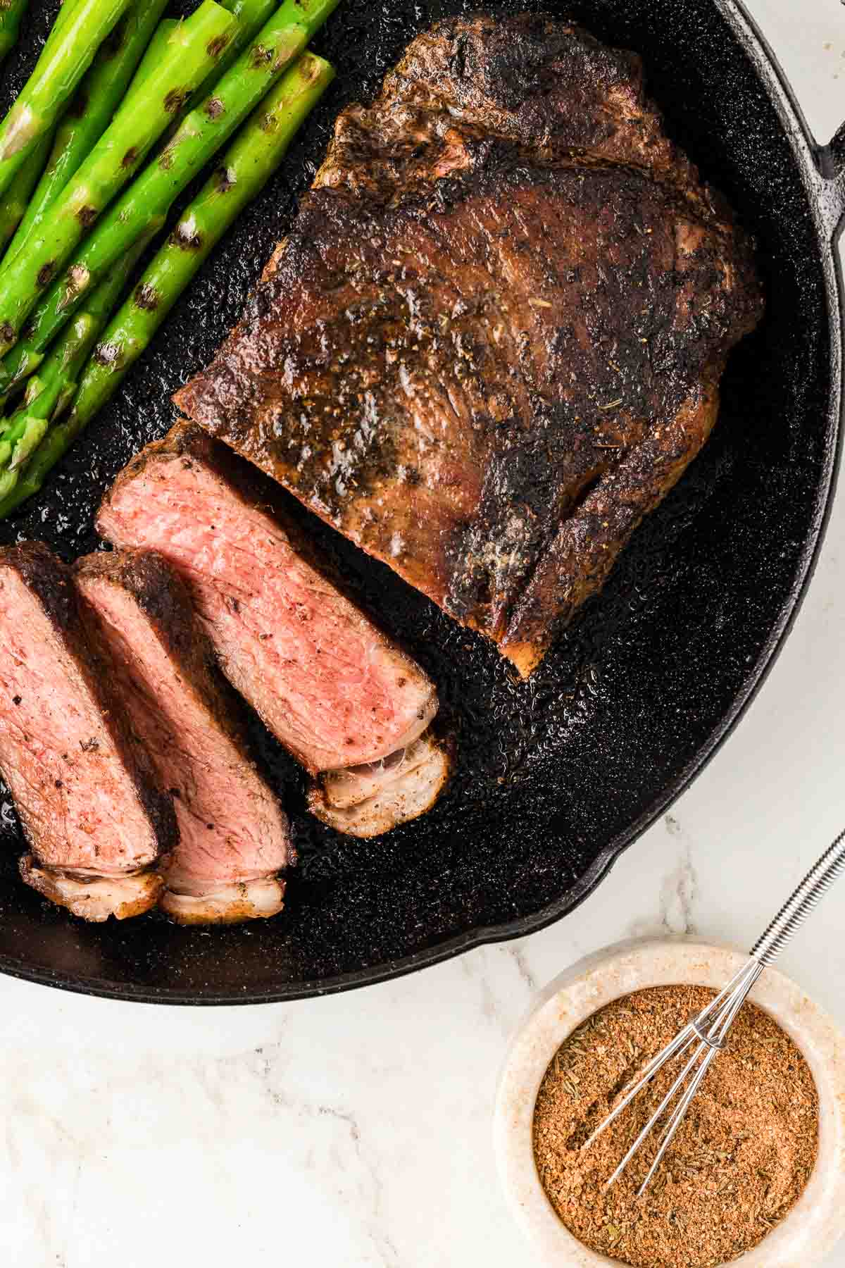 Blackened steak sliced and asparagus in a cast iron skillet.