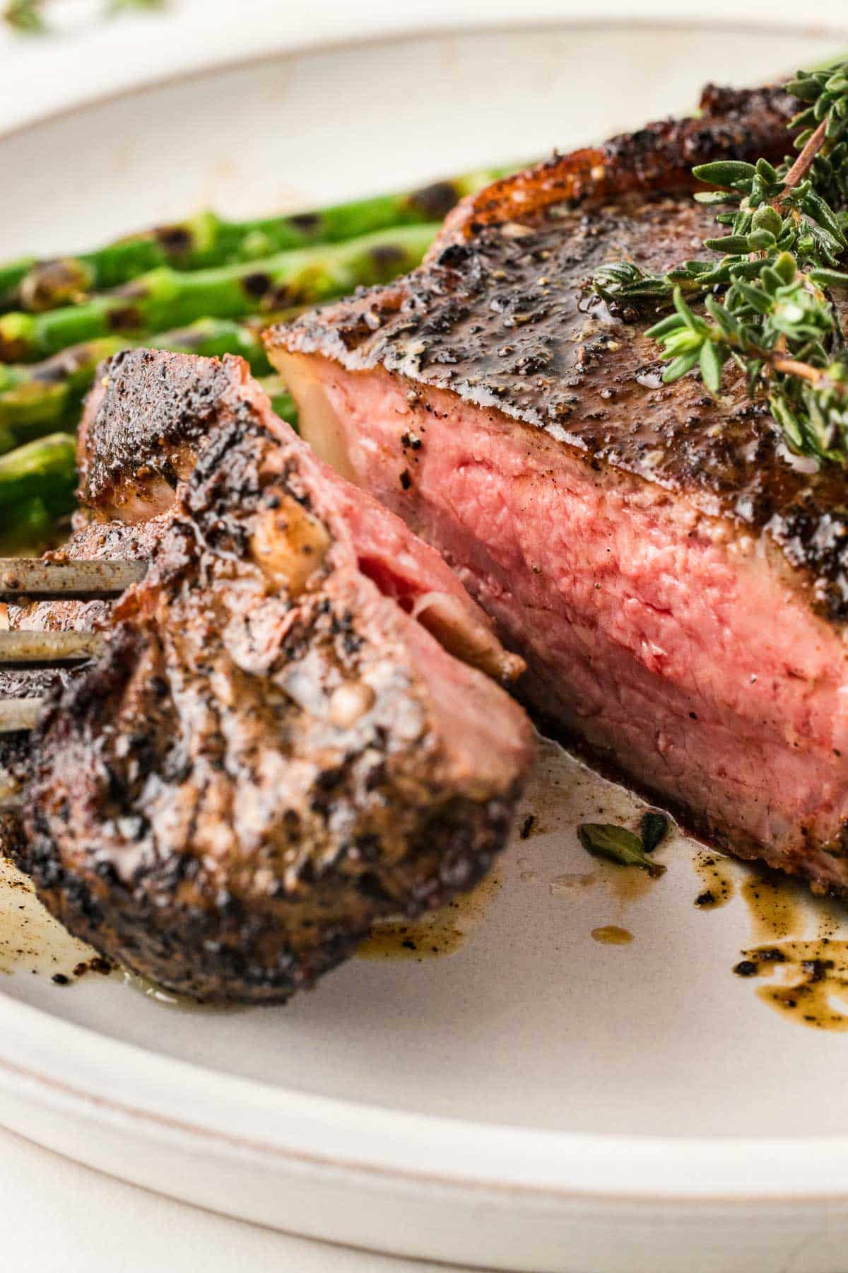A blackened steak with asparagus and herbs on a plate.
