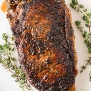 A blackened steak on a white plate with thyme sprigs.