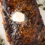 A blackened steak with butter and thyme on a plate.