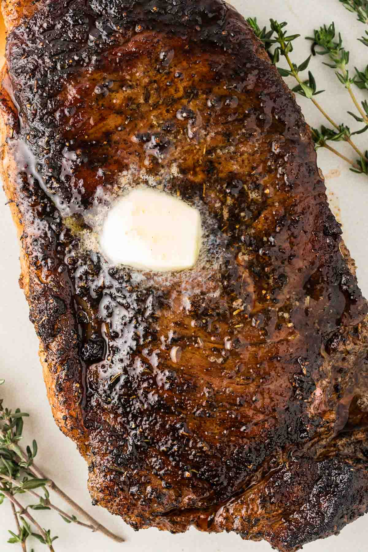 A blackened steak with butter and thyme on a plate.