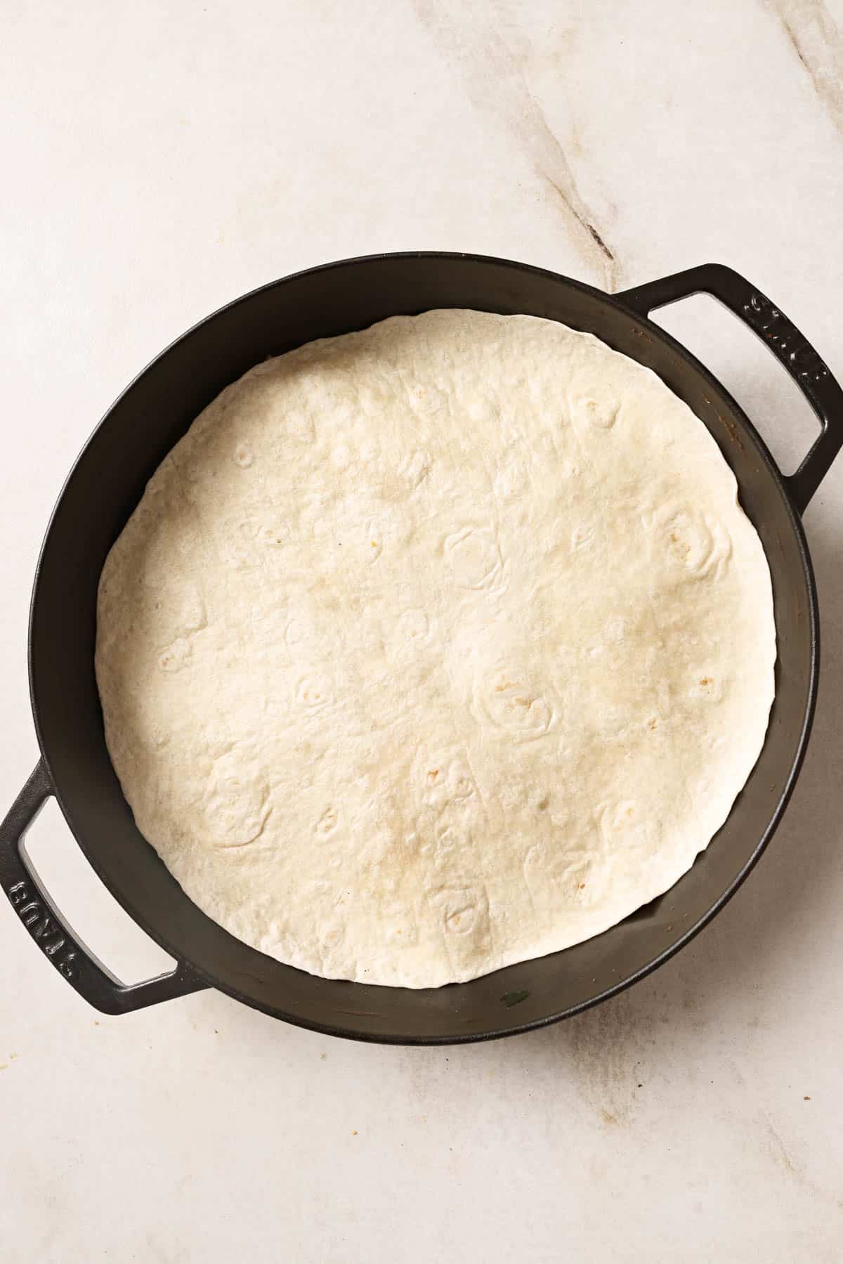 A tortilla in a cast iron pan on a marble countertop.