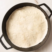 A tortilla tops a quesadilla in a cast iron pan on a marble countertop.