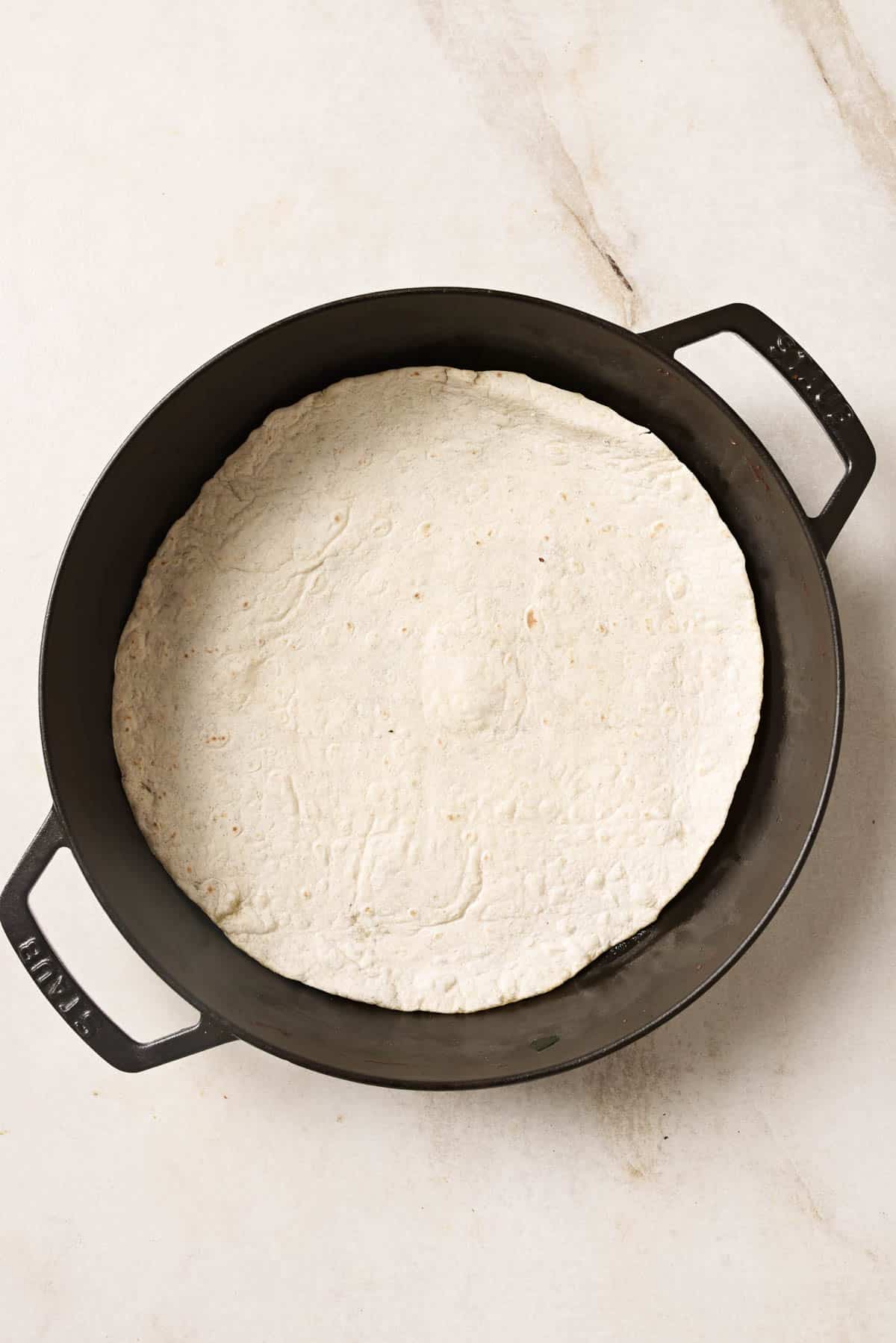 A tortilla in a cast iron pan on a white surface.