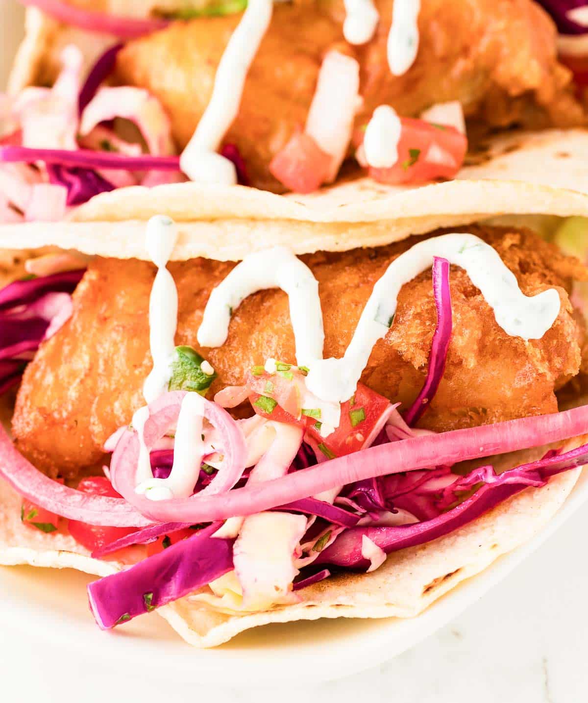 Beer-battered fish tacos with red cabbage slaw and a drizzle of creamy sauce.
