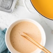 A bowl of liquid batter with chopsticks in it next to a pot of oil.