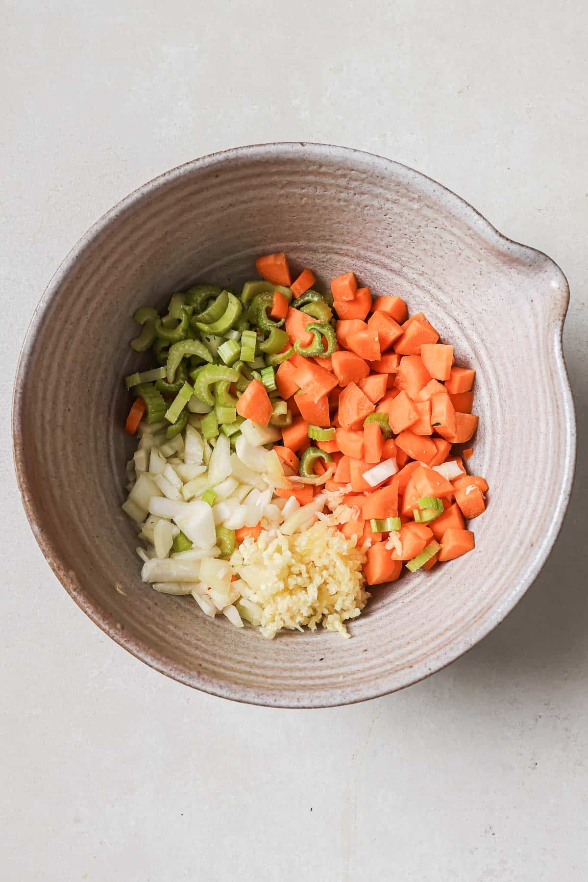 Chopped carrots, celery, onions, and garlic in a bowl, ingredients prepared for cooking.