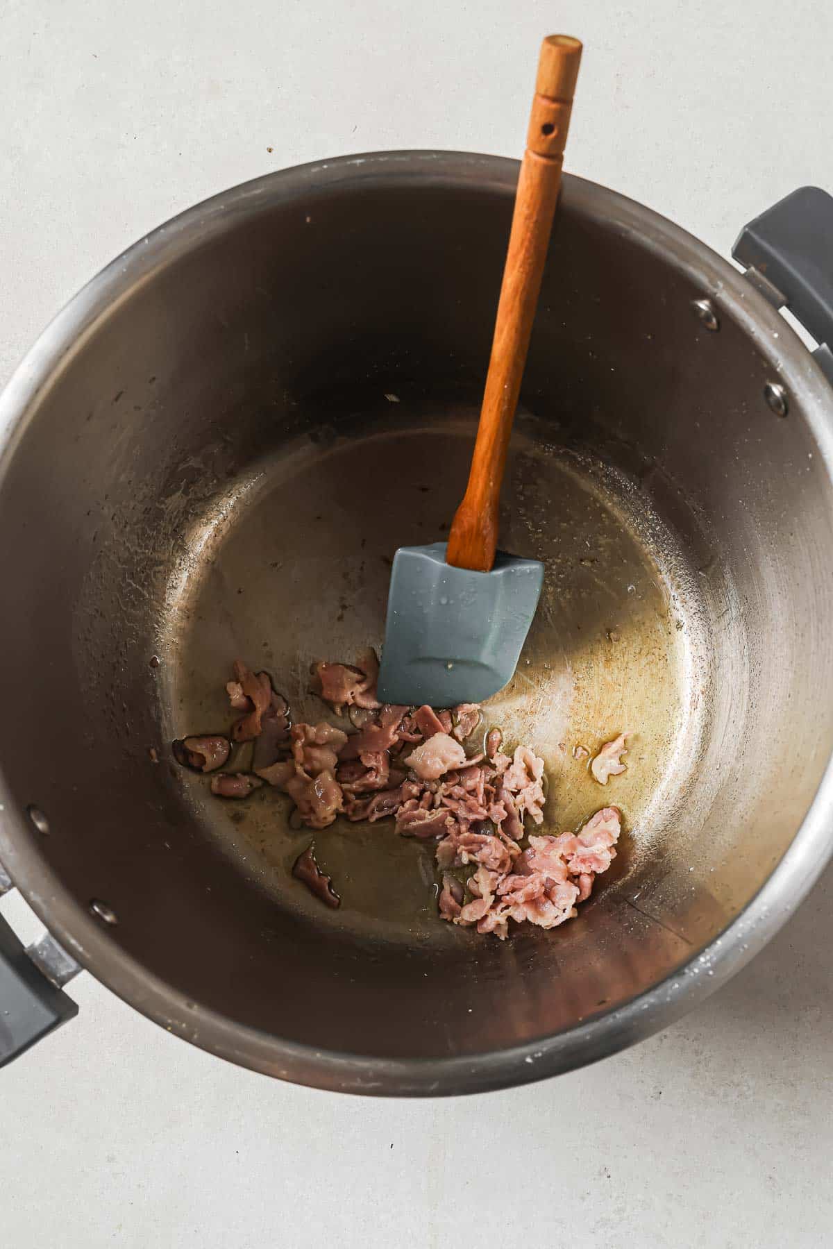 A pot with cooked bacon pieces and a silicone spatula.