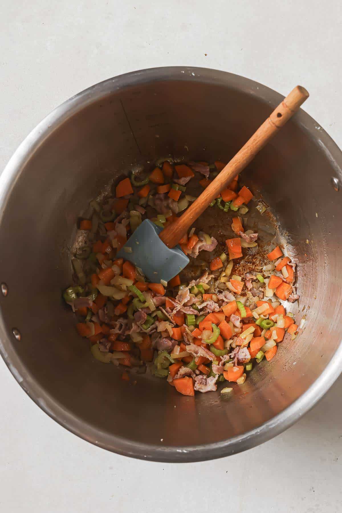 Diced vegetables with a wooden spatula in a stainless steel cooking pot.