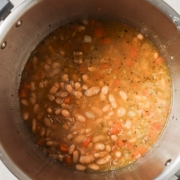 A Instant pot containing cooked navy beans and diced vegetables with broth.