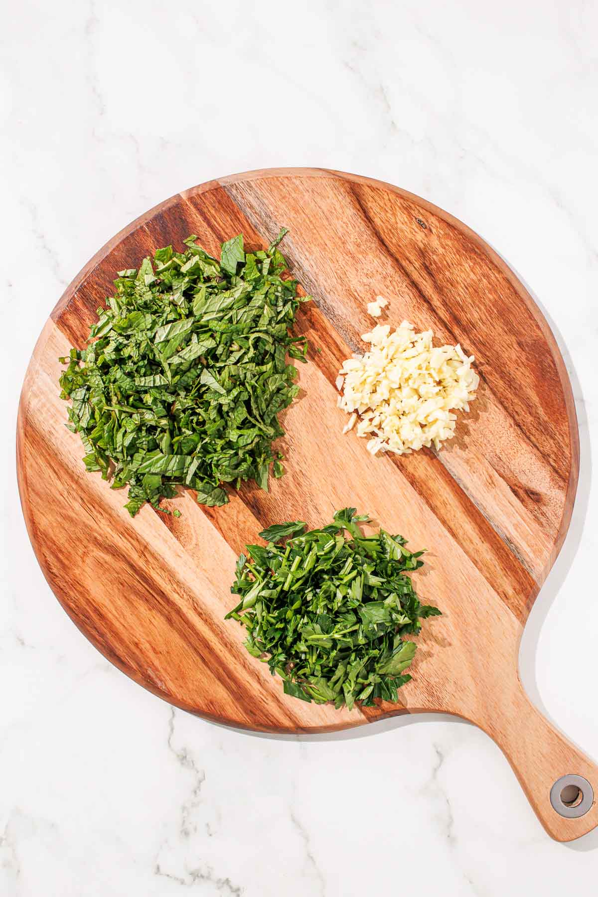 Minced garlic and chopped herbs on a wooden cutting board.