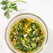 Top view of a glass jar filled with mint chimichurri, placed on a white marble surface.