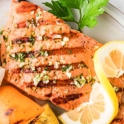 Grilled sockeye salmon fillet garnished with lemon slices and parsley, served with grilled vegetables including bell pepper, zucchini, mushroom, and red onion.