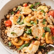 A bowl of quinoa topped with sliced chicken, chickpeas, cherry tomatoes, yellow squash, and fresh basil.