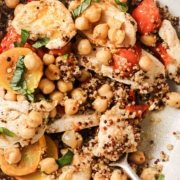 A bowl of quinoa salad with chickpeas, sliced chicken breast, cherry tomatoes, and fresh basil, with a fork resting on the side.