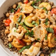 A bowl of quinoa topped with sliced chicken breast, chickpeas, zucchini, yellow squash, cherry tomatoes, and fresh basil.