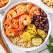 A bowl with quinoa, cooked shrimp, black beans, and sautéed slices of yellow squash and zucchini.